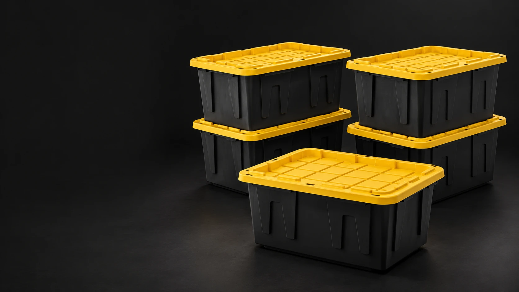 Black moving totes with yellow lids stacked on a dark studio floor.